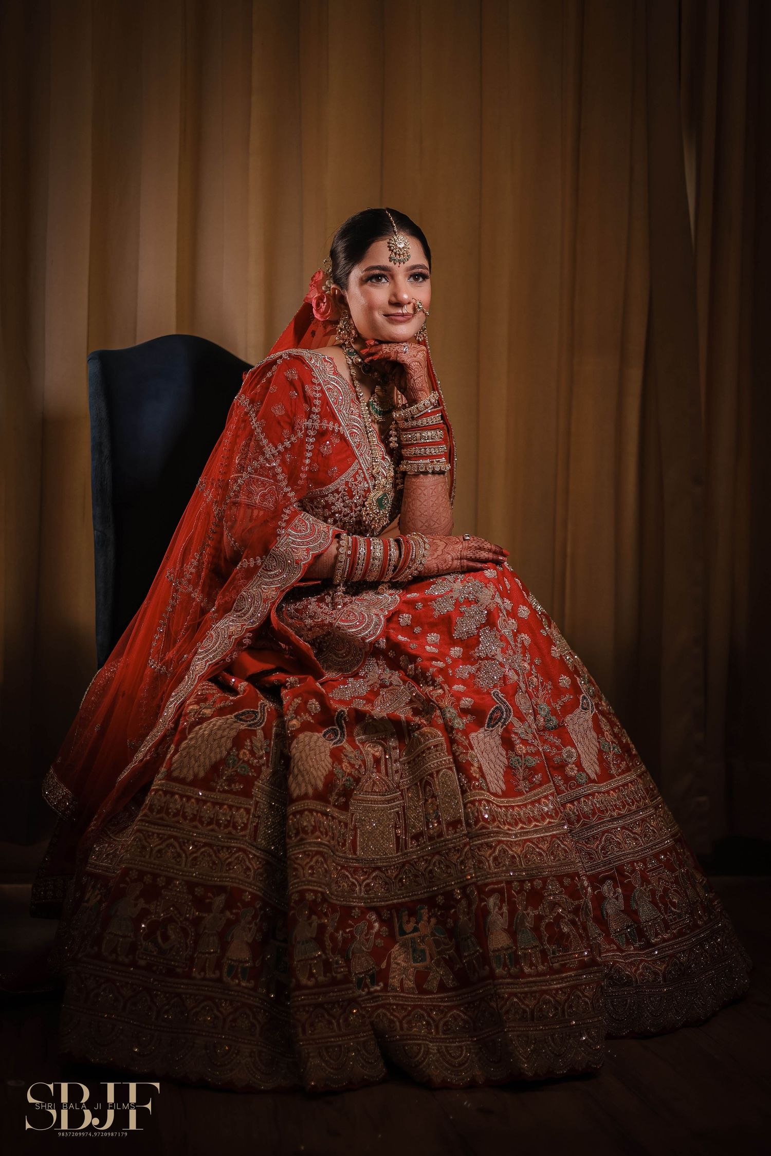 Traditional Indian bridal attire featuring an ornate red lehenga with intricate embroidery and matching veil in moody lighting.