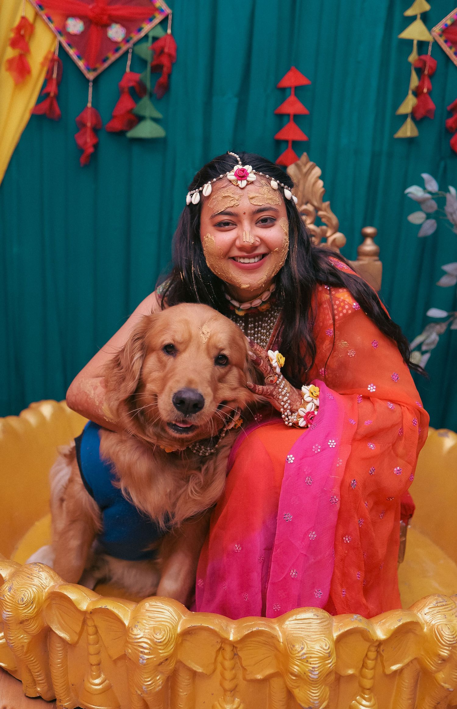 Golden retriever and person in bright festive attire pose against decorated turquoise backdrop.