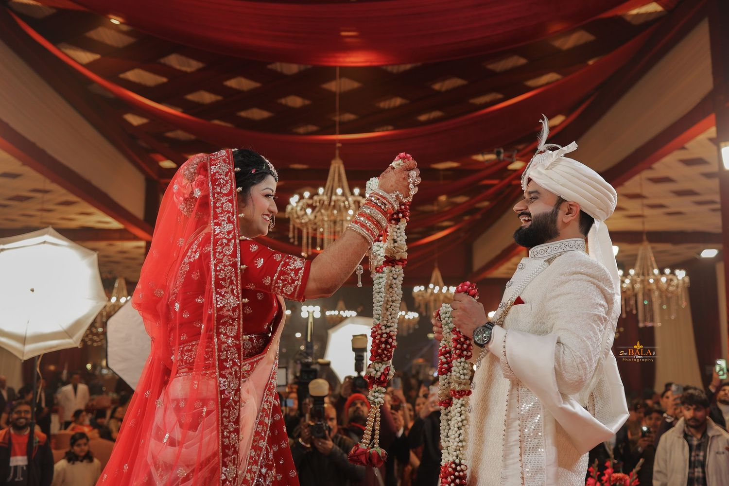 A couple wearing traditional South Asian wedding attire performs a celebratory ritual during their wedding ceremony.