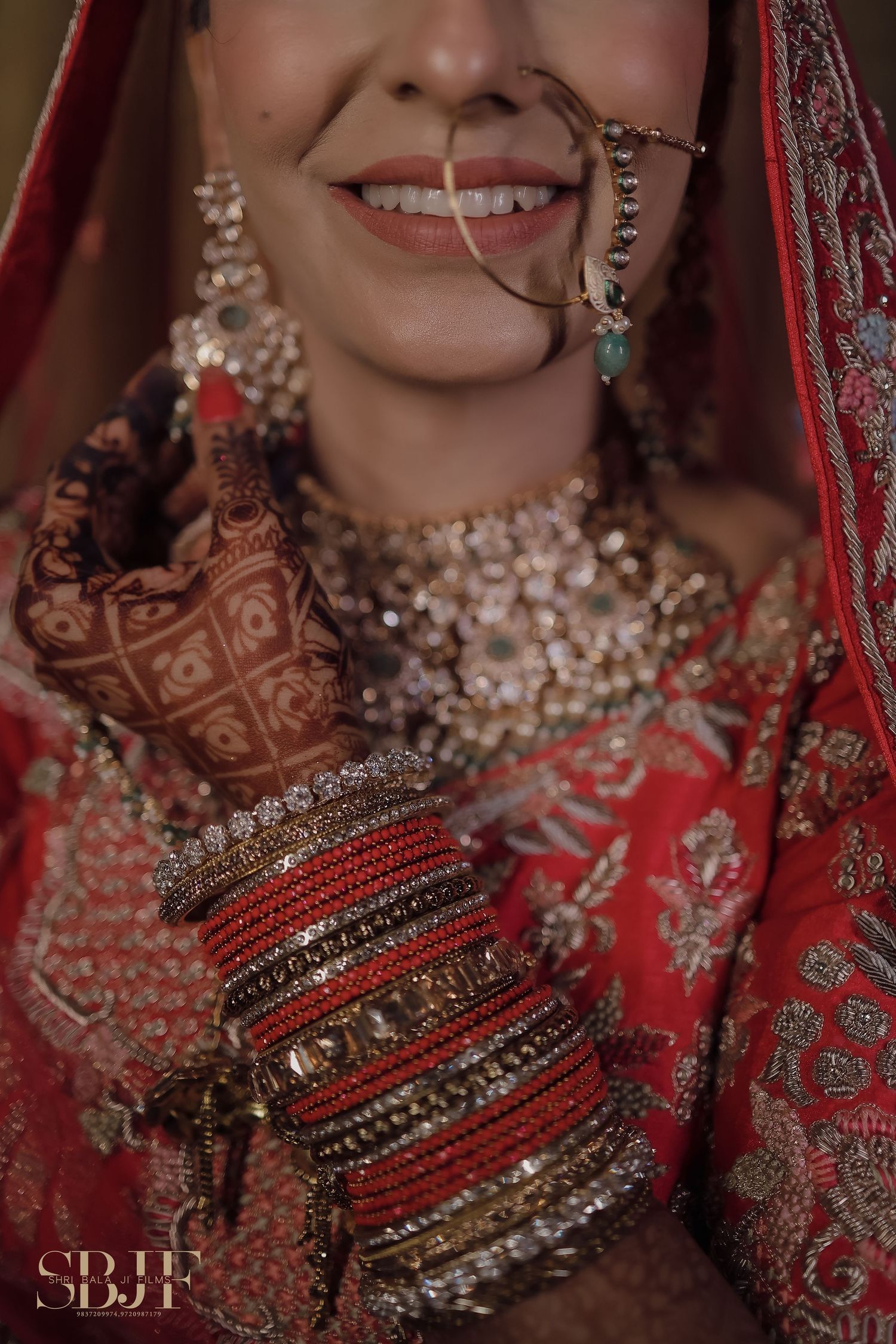 Close-up of traditional Indian bridal jewelry and red lehenga with intricate embroidery and stacked bangles.