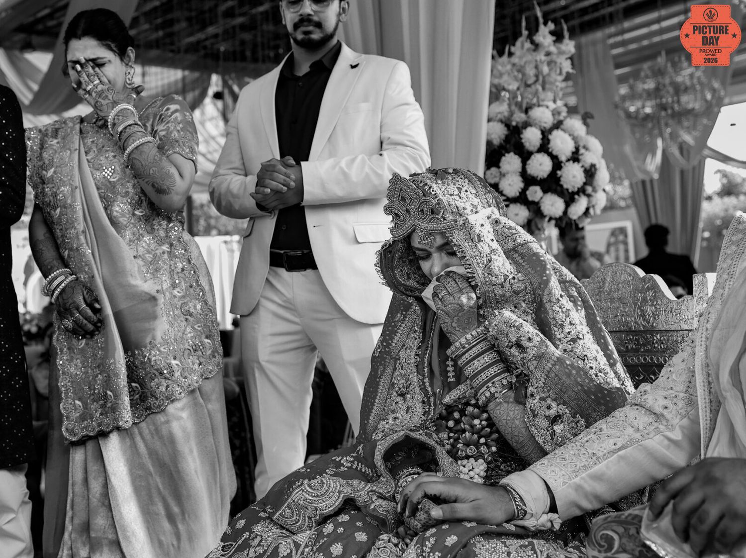 Black and white photo of a bride in ornate jewelry at a traditional Indian wedding ceremony.