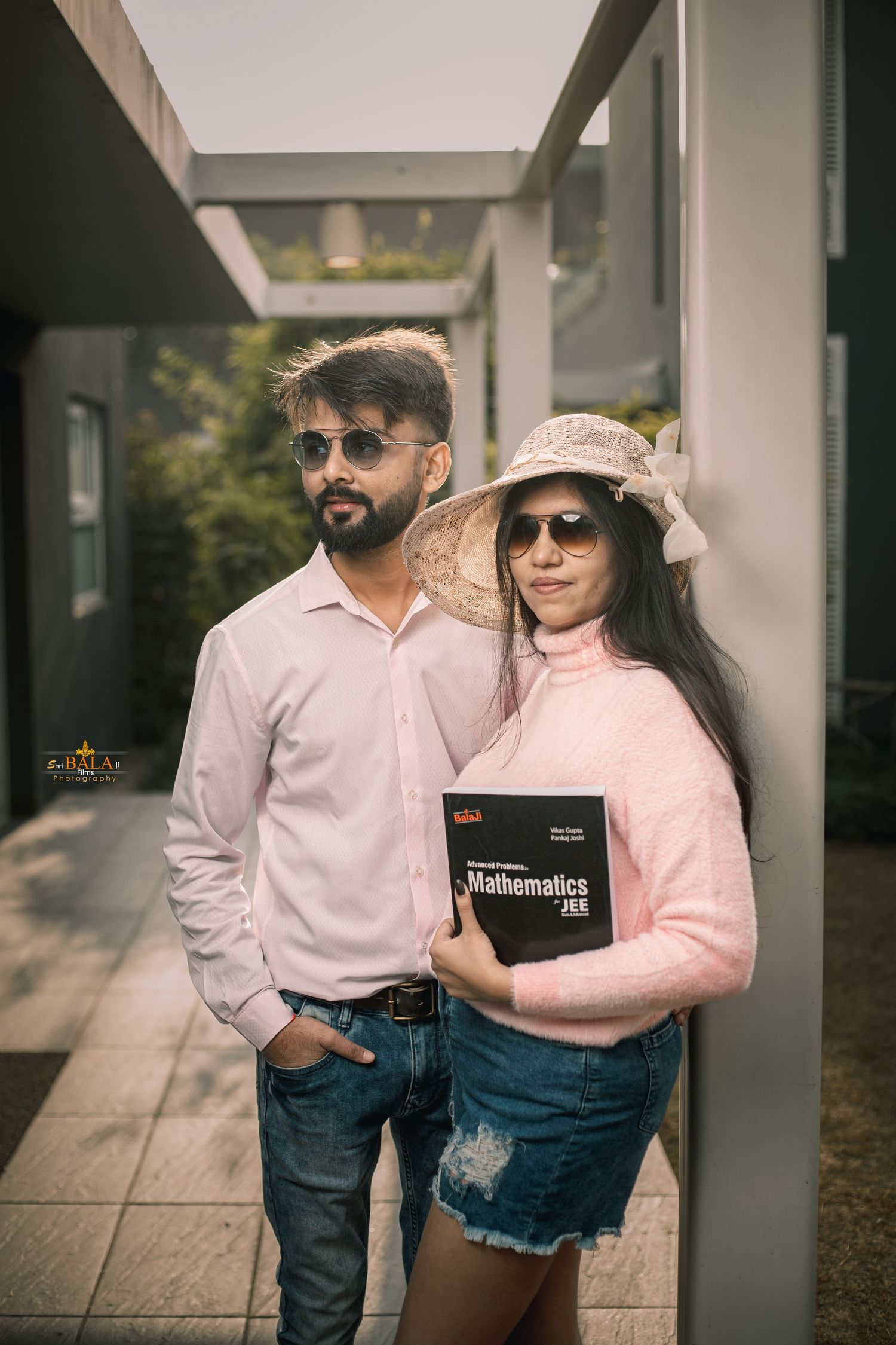 Couple in casual wear posing with books against white pillared backdrop.