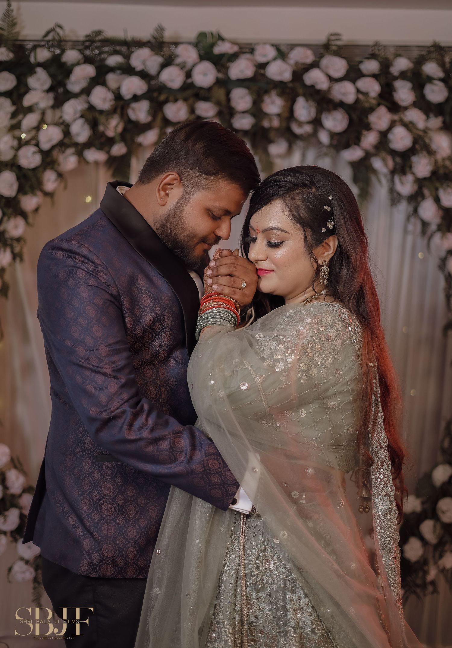 Romantic wedding couple embraces in front of floral arch backdrop with blush roses and white flowers at elegant reception.