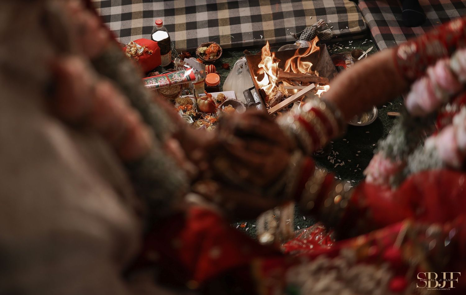 Blurred hands in front frame a cozy fireplace with warm flames and holiday decorations.