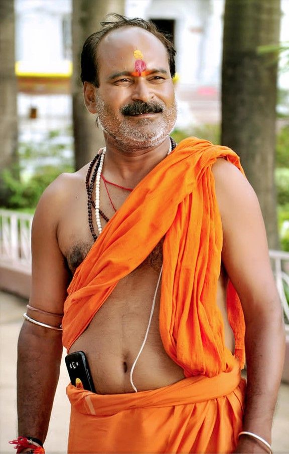 Person in saffron colored traditional dress with religious markings photographed near pillars.