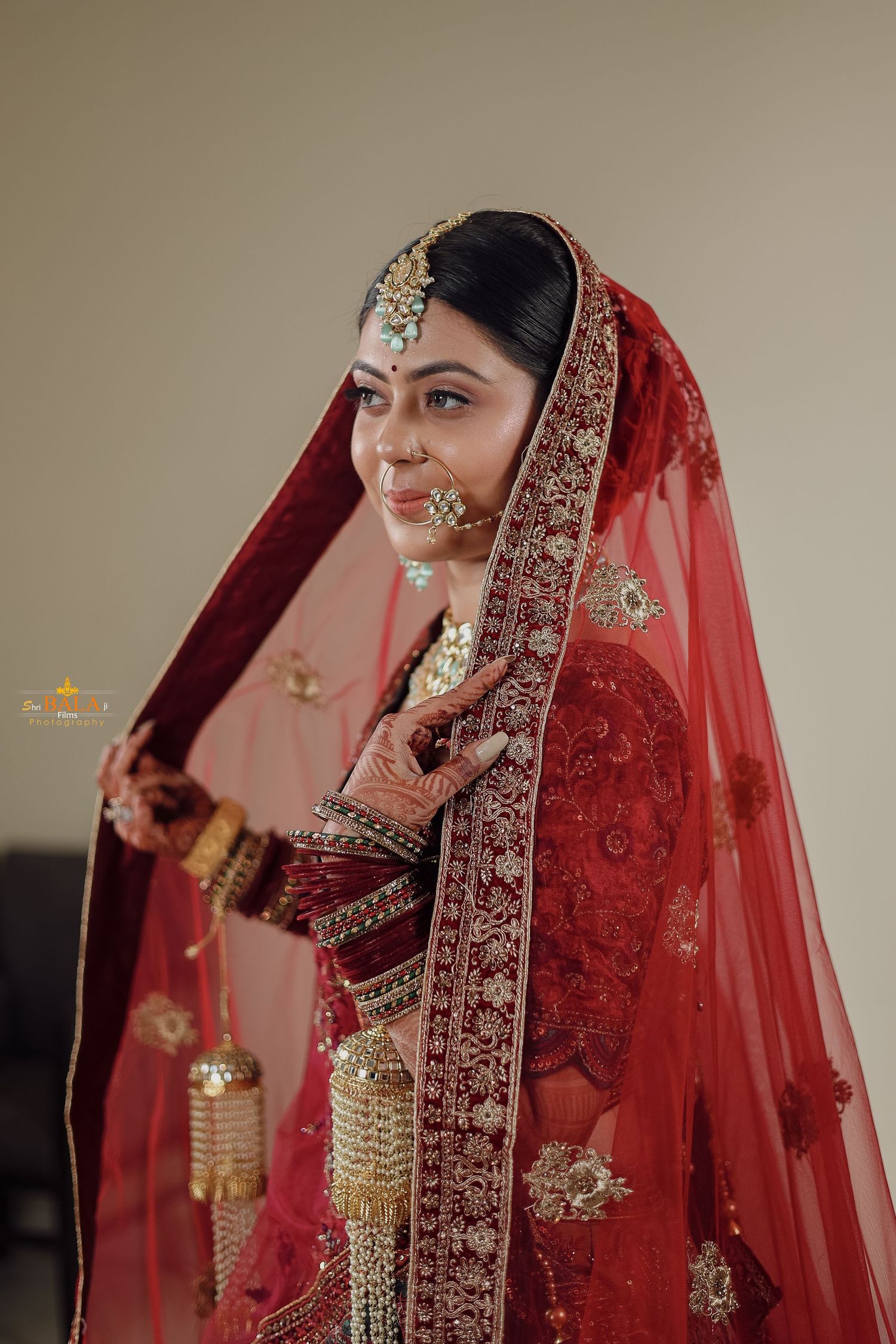 A bride in a traditional red embroidered lehenga and veil adorned with intricate golden jewelry and ornaments.