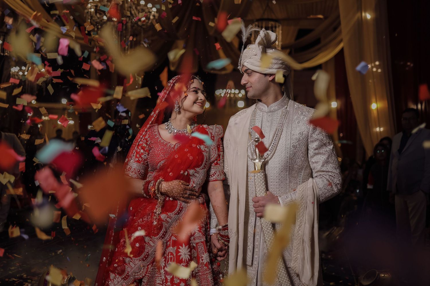 People in formal attire dance and celebrate at an elegant evening reception with glowing lights in the background.
