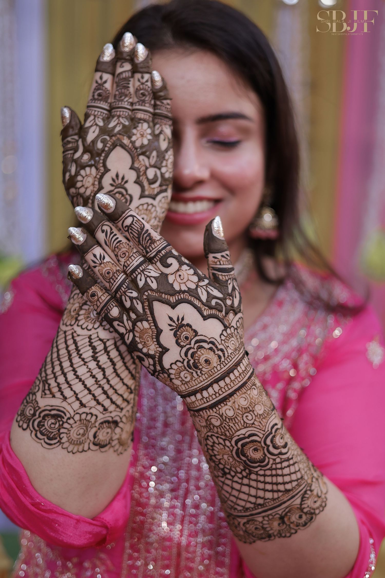 Close-up view of intricate bridal mehndi designs showing detailed peacock and floral patterns on hands against pink attire.