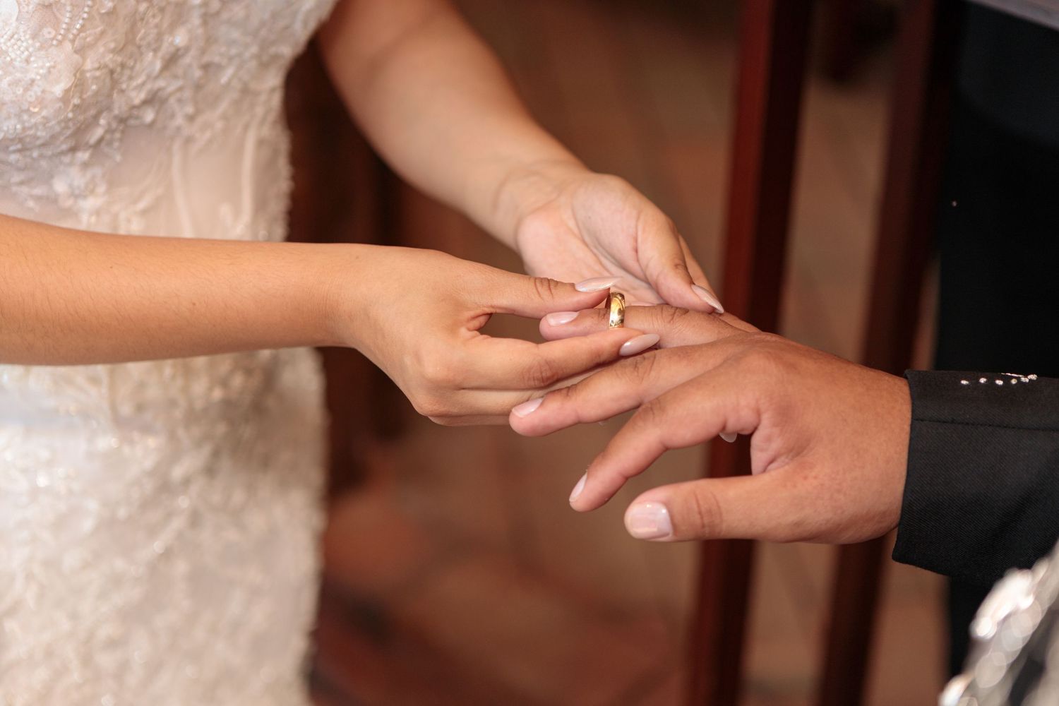 Close-up of bride placing gold wedding ring on grooms finger during wedding ceremony.