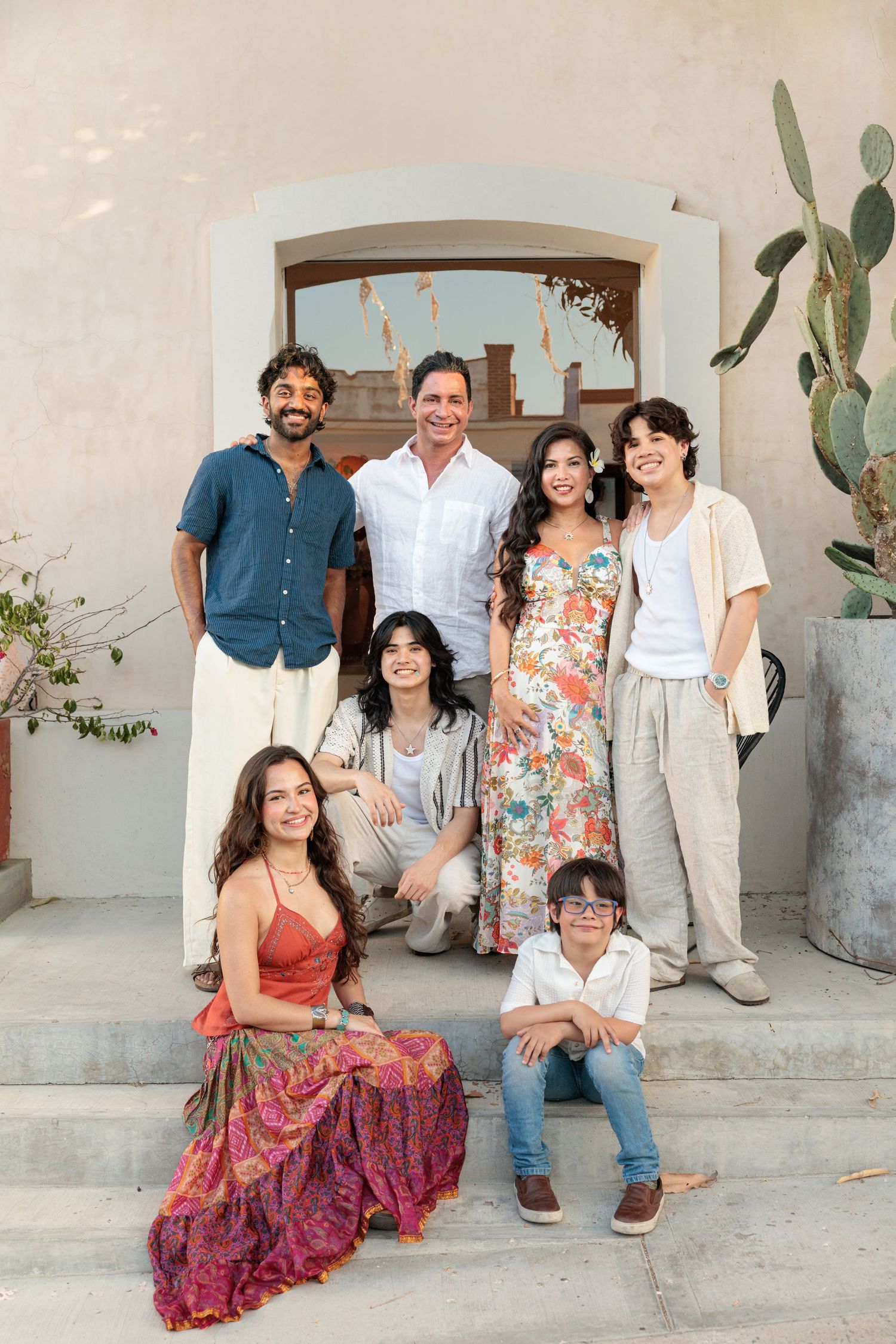 A joyful multigenerational family poses together on stone steps outside a Mediterranean-style building.
