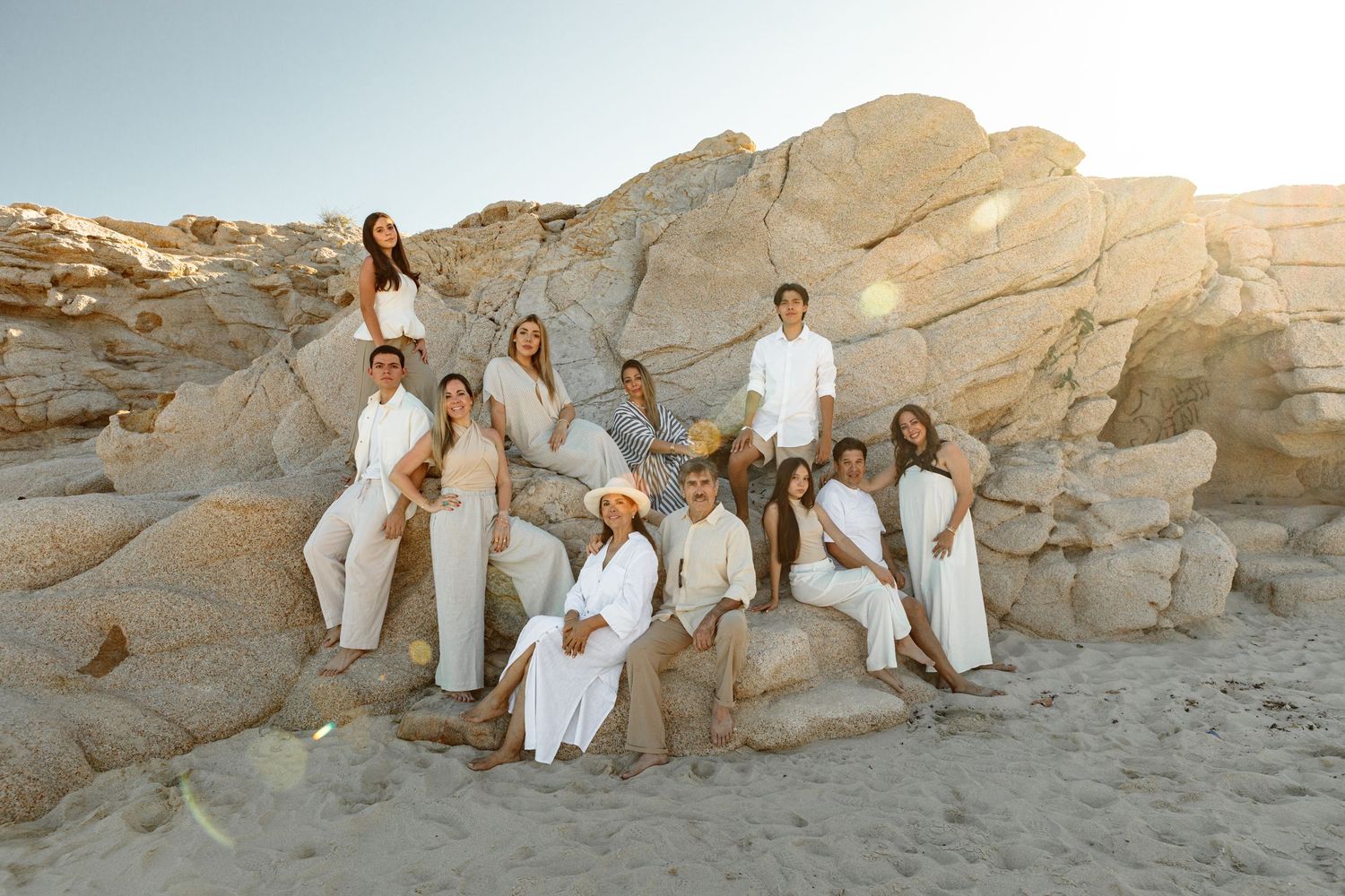 Large family group poses on rocky beach in coordinated white and beige outfits.