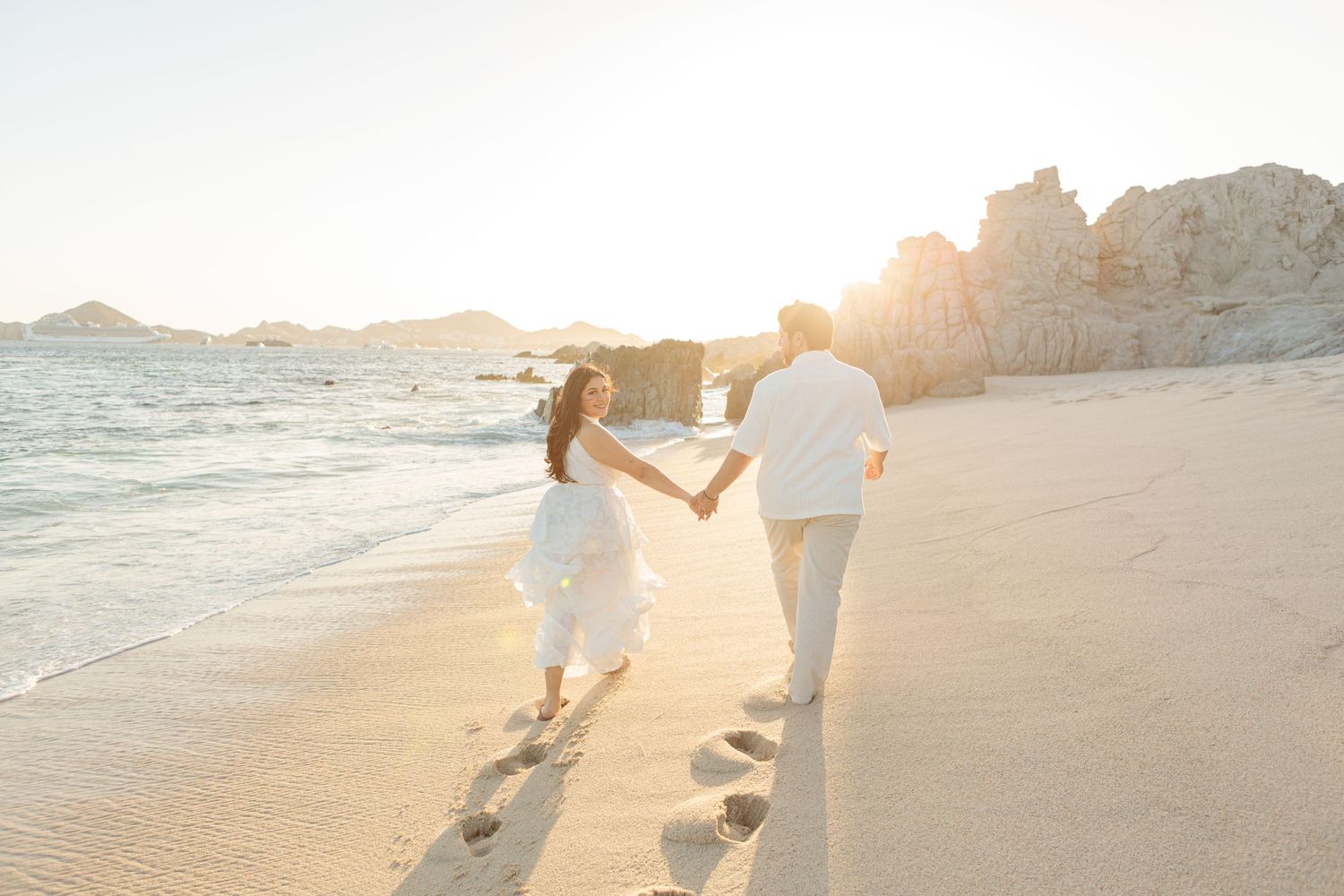 Couple walking hand in hand, along the beach, during a romantic sunset photo session in Los Cabos.