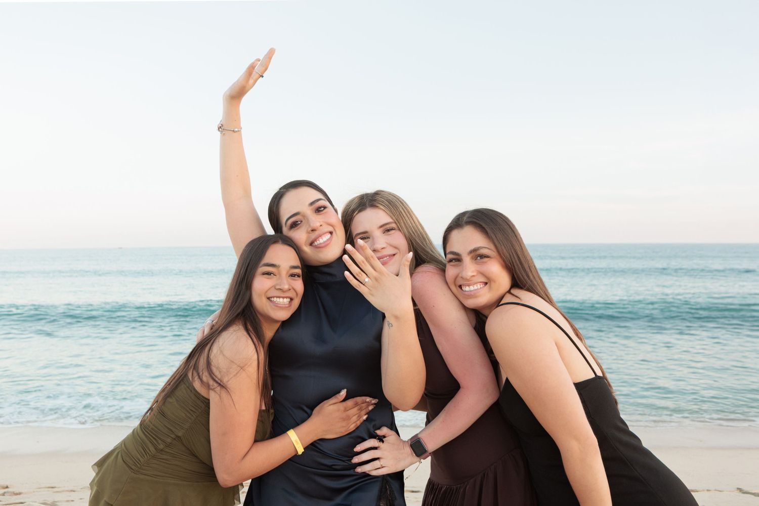 Four women celebrating a beach engagement, one showing off her diamond ring.