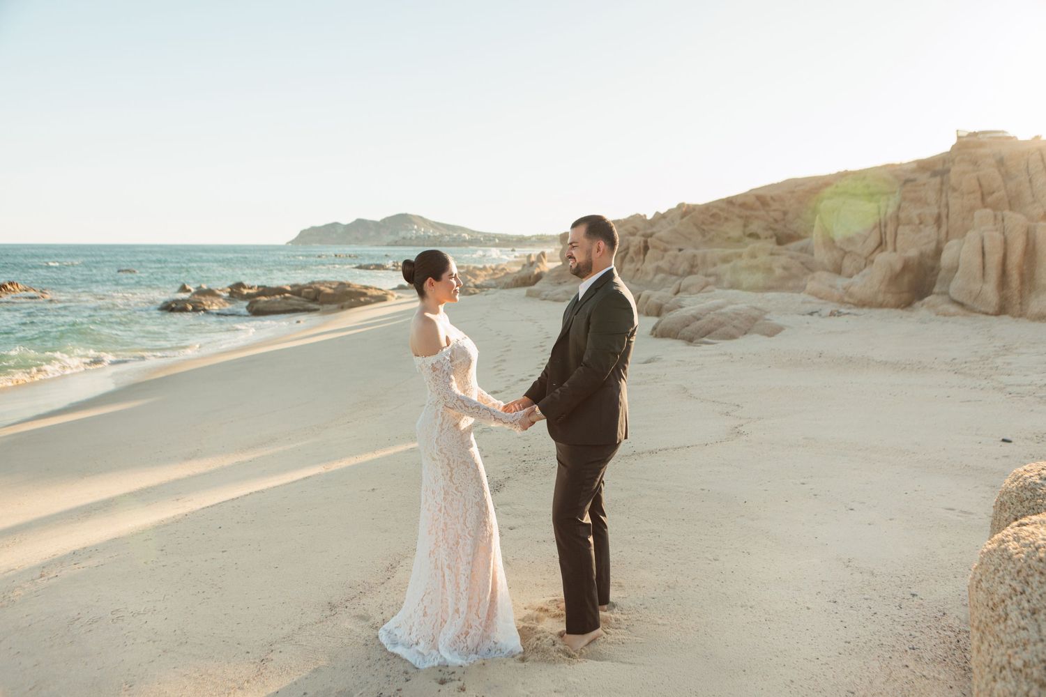 Bride and groom holding hands on a sandy beach at golden hour during their destination wedding.