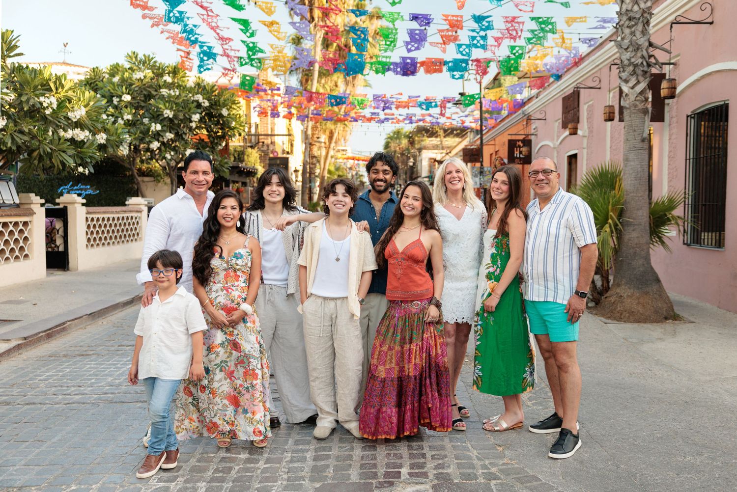 Group of people posing on a colorful street decorated with vibrant papel picado banners overhead.