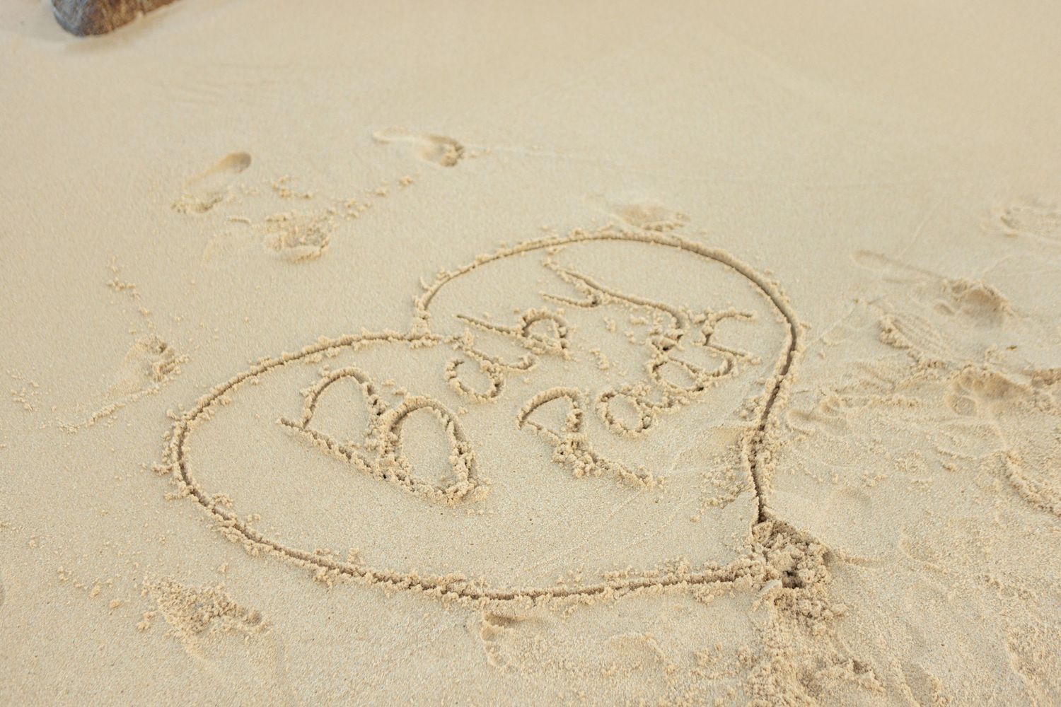Heart shape with baby footprints drawn in smooth golden sand on a serene beach.