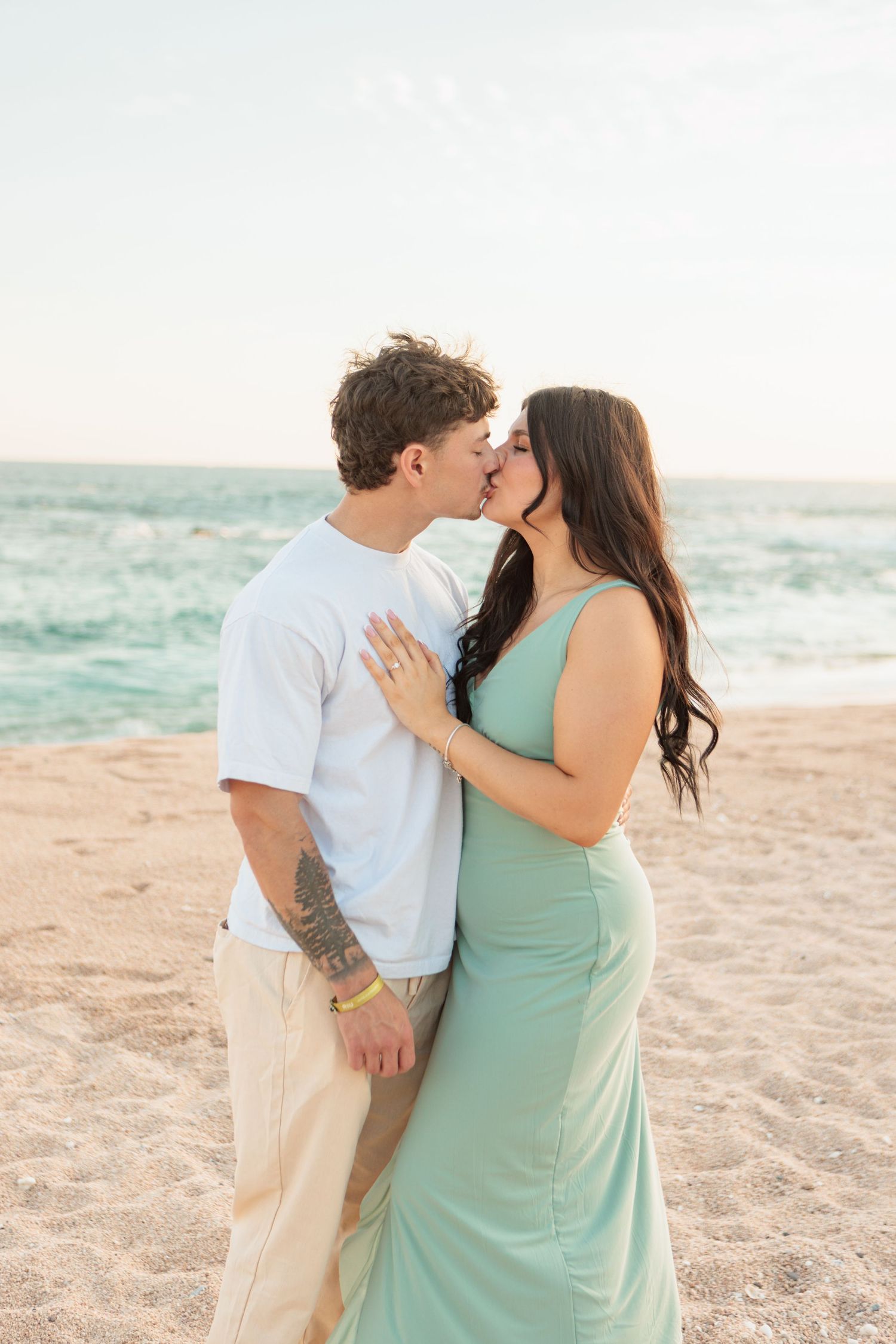 Newly engaged couple kissing on beach showing engagement ring at golden hour.