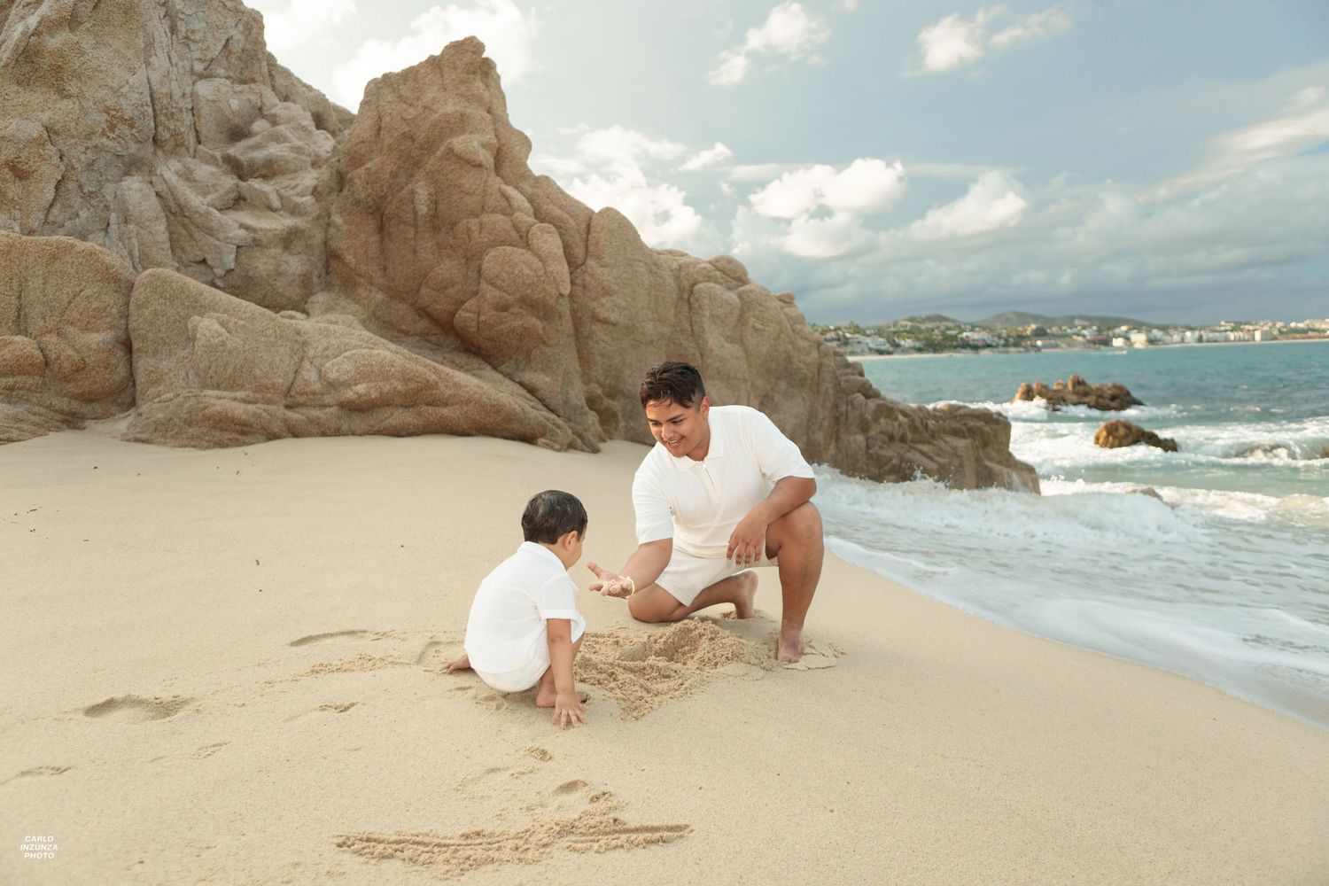 Father and young child playing in the sand together on a scenic rocky beach with ocean waves.