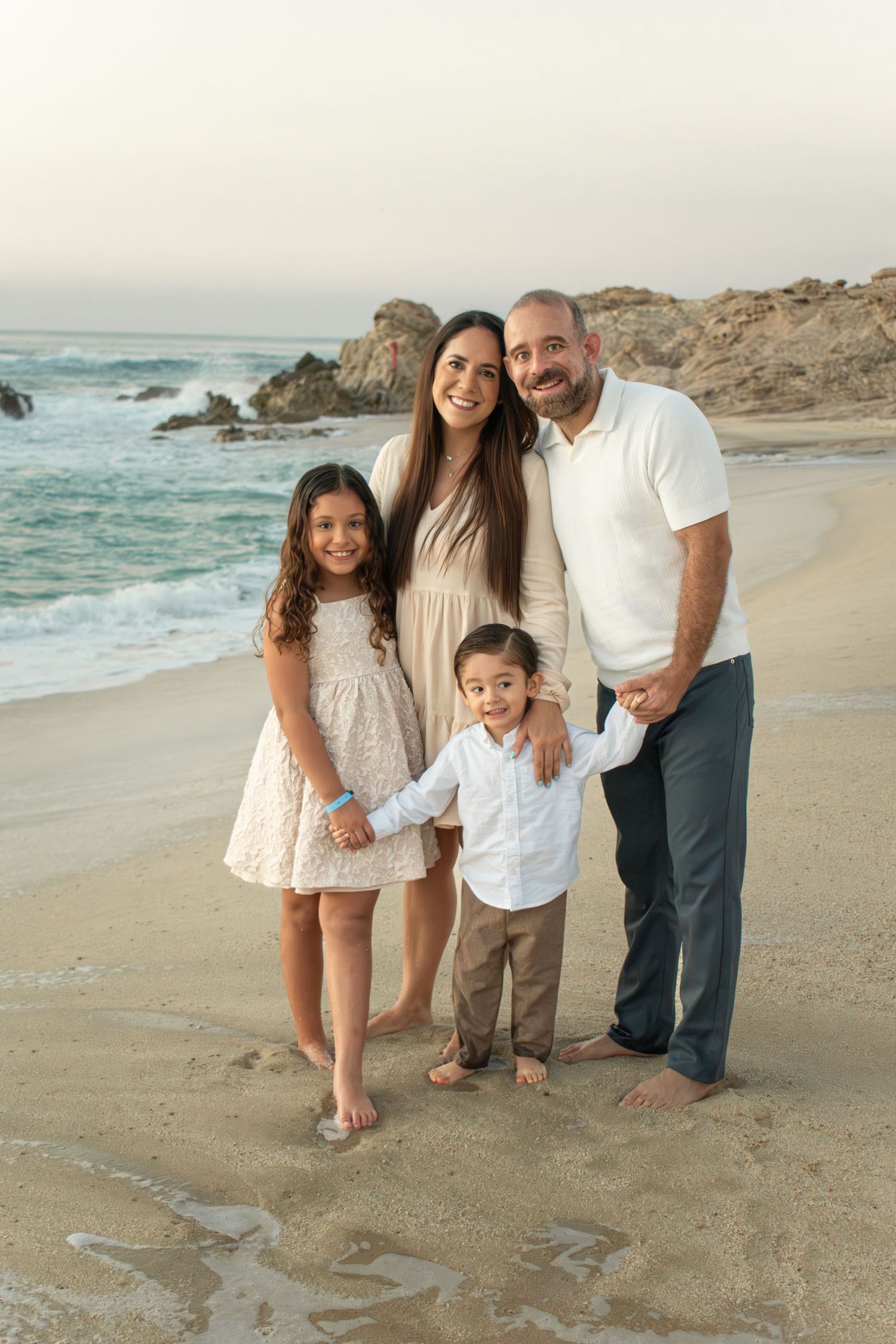 Happy family of four posing together on rocky beach shore at golden hour.