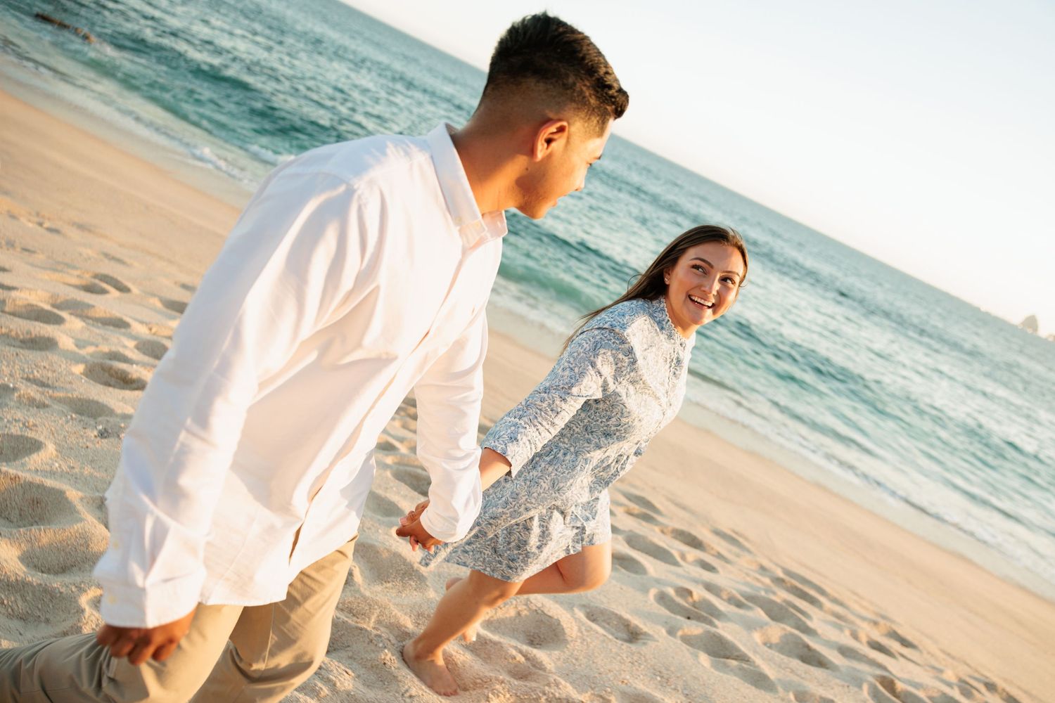 Happy couple holding hands and running along a sunny beach with turquoise ocean waves.