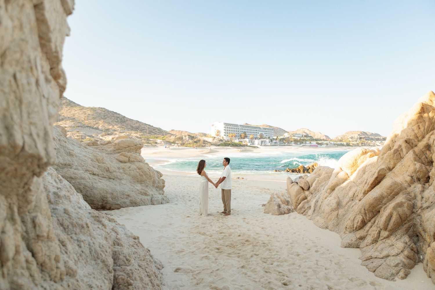 Couple holds hands between white rock formations on a scenic beach.