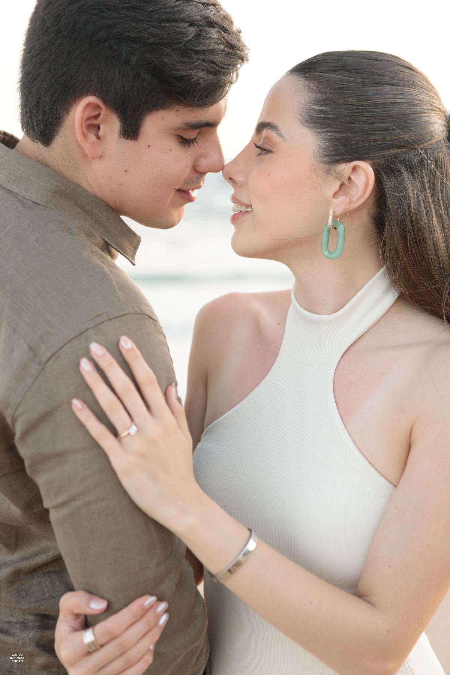 Romantic couple almost kissing closeup, woman wearing white halter dress and turquoise earrings with engagement ring.