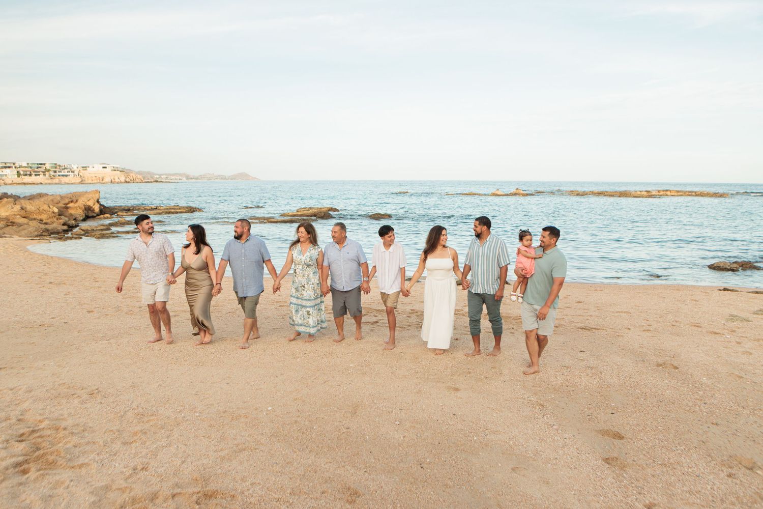 Extended family holding hands and walking along a sunny beach together.