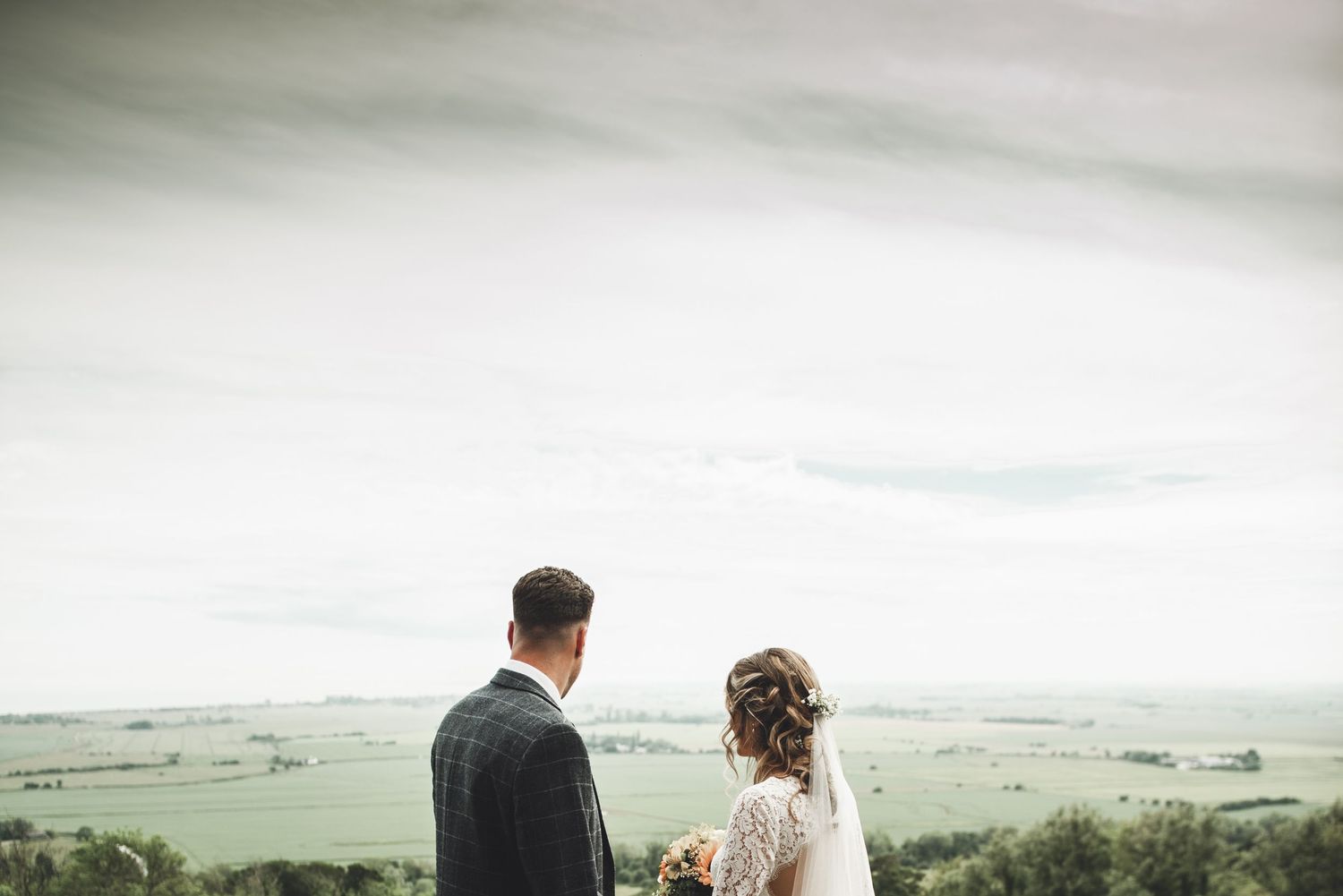 Couple stood on grassy cliffside enjoy sweeping views over the rugged ocean coastline on a misty day.