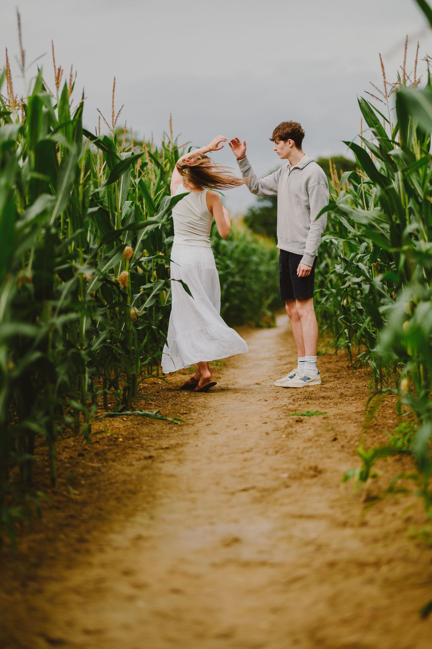 People walking and playing together on a dirt path between tall green corn stalks in a cornfield during golden hour.