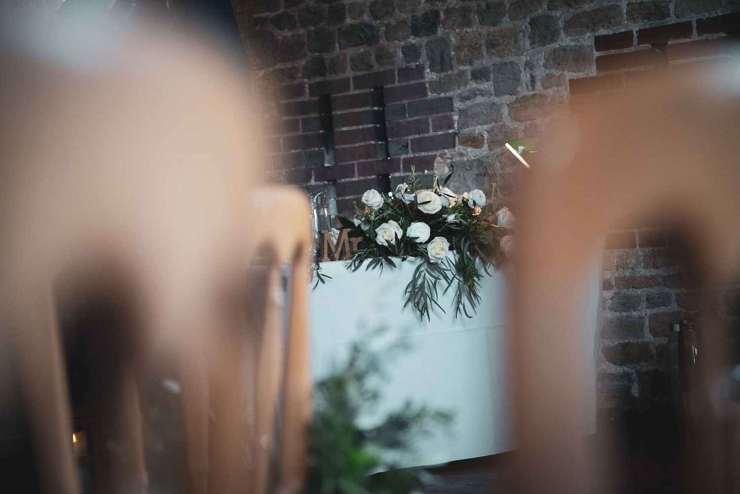White floral arrangement with greenery against exposed brick wall.