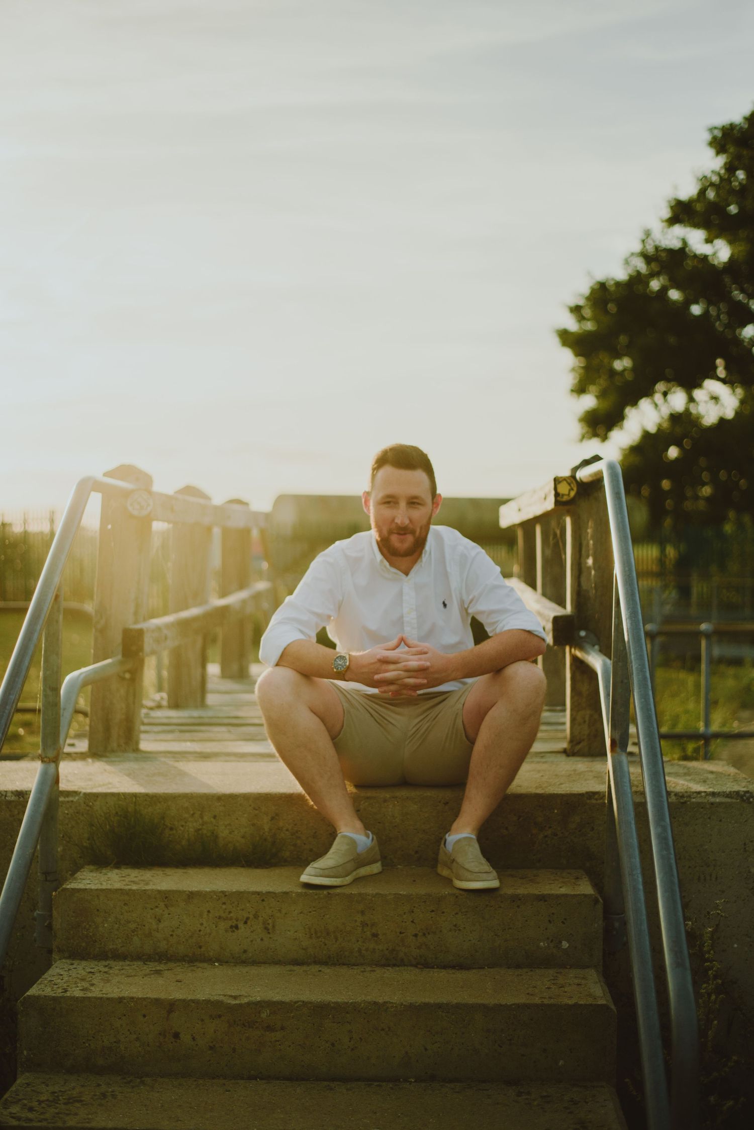 Person sitting alone on concrete steps at sunset with metal railings.