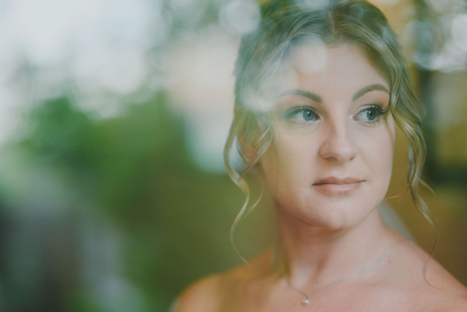 A soft focus portrait with a dreamy bokeh effect shows someone with blonde hair smiling against a blurred green background.