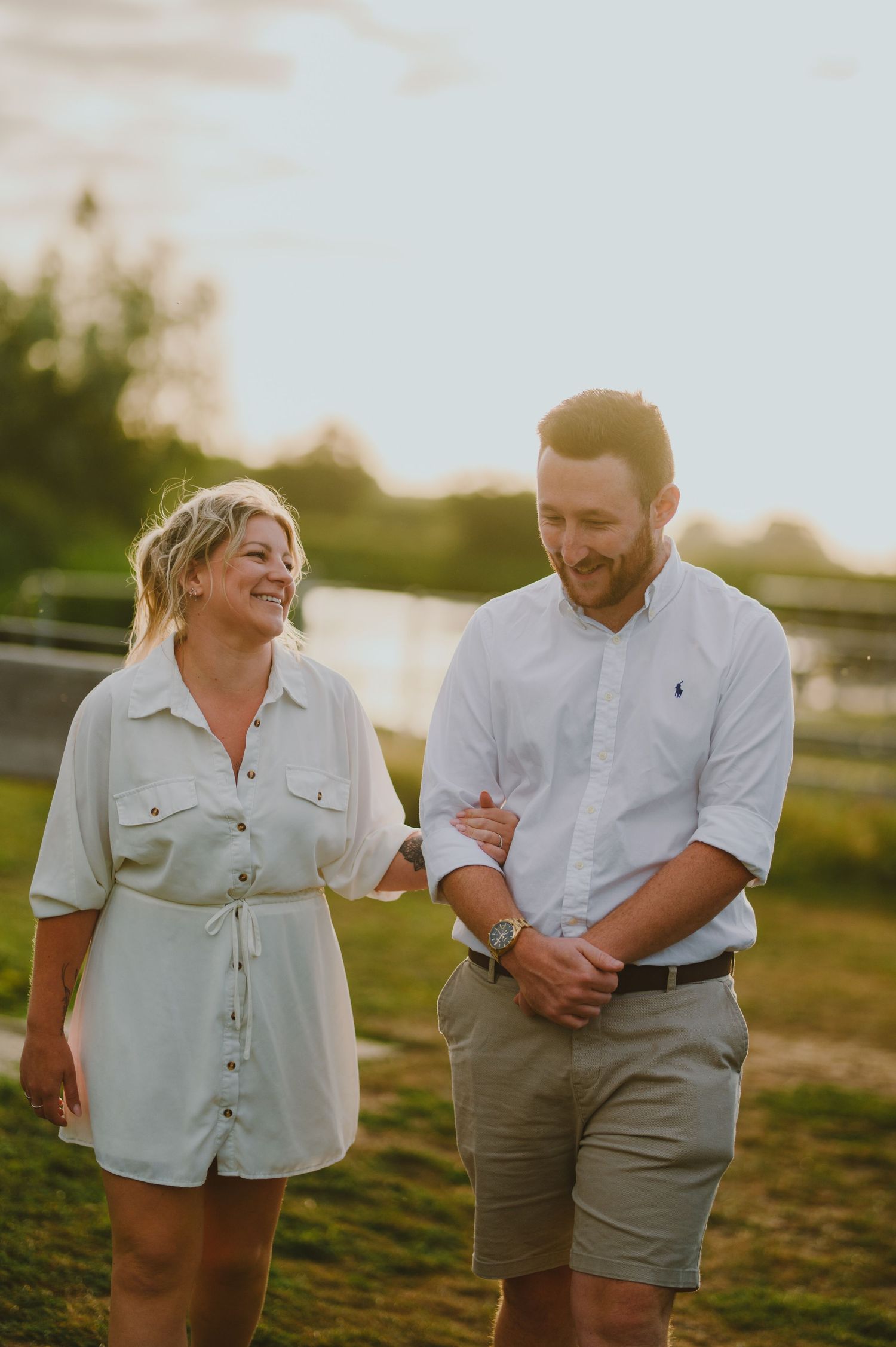 A couple shares a candid laughing moment together outdoors during golden hour sunset lighting.