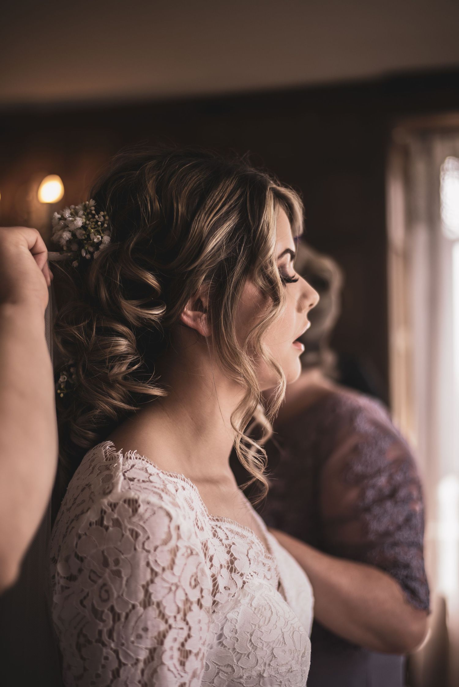 Close up detail of delicate white lace wedding dress in soft indoor lighting.
