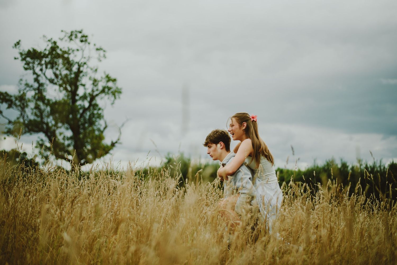 A loving moment captured in a golden wheatfield under moody skies with tall grasses swaying in the breeze.