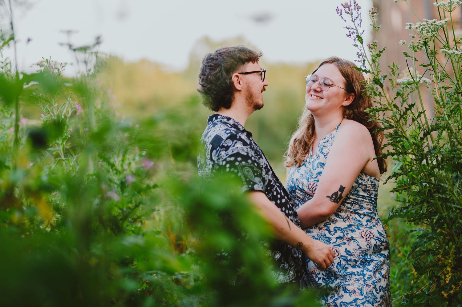 A couple shares a joyful moment together in a lush garden setting surrounded by green foliage and flowers.