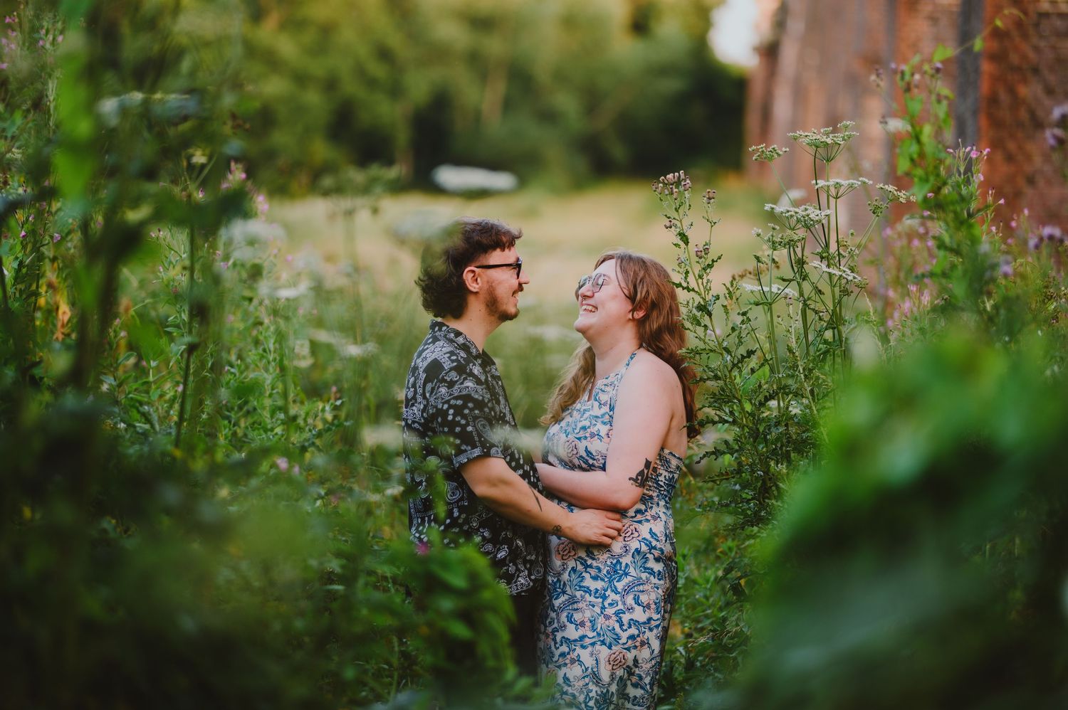 Two people share a tender moment together in a lush summer garden surrounded by blooming flowers and greenery.