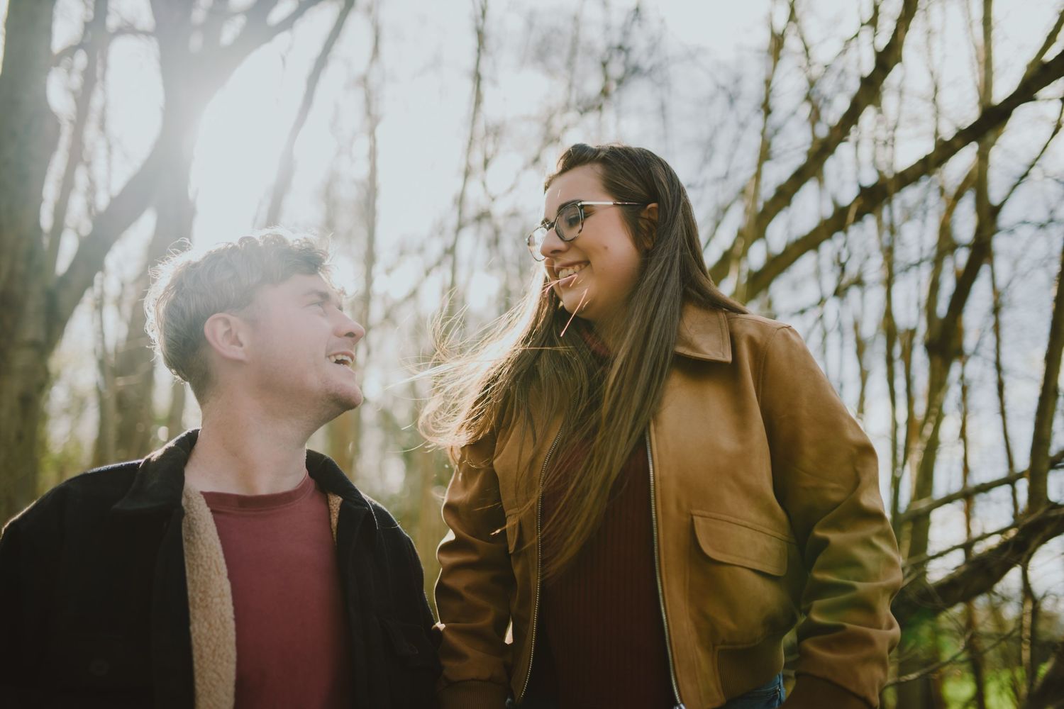 A young couple laughs together while walking outdoors on a misty autumn day in casual outerwear.
