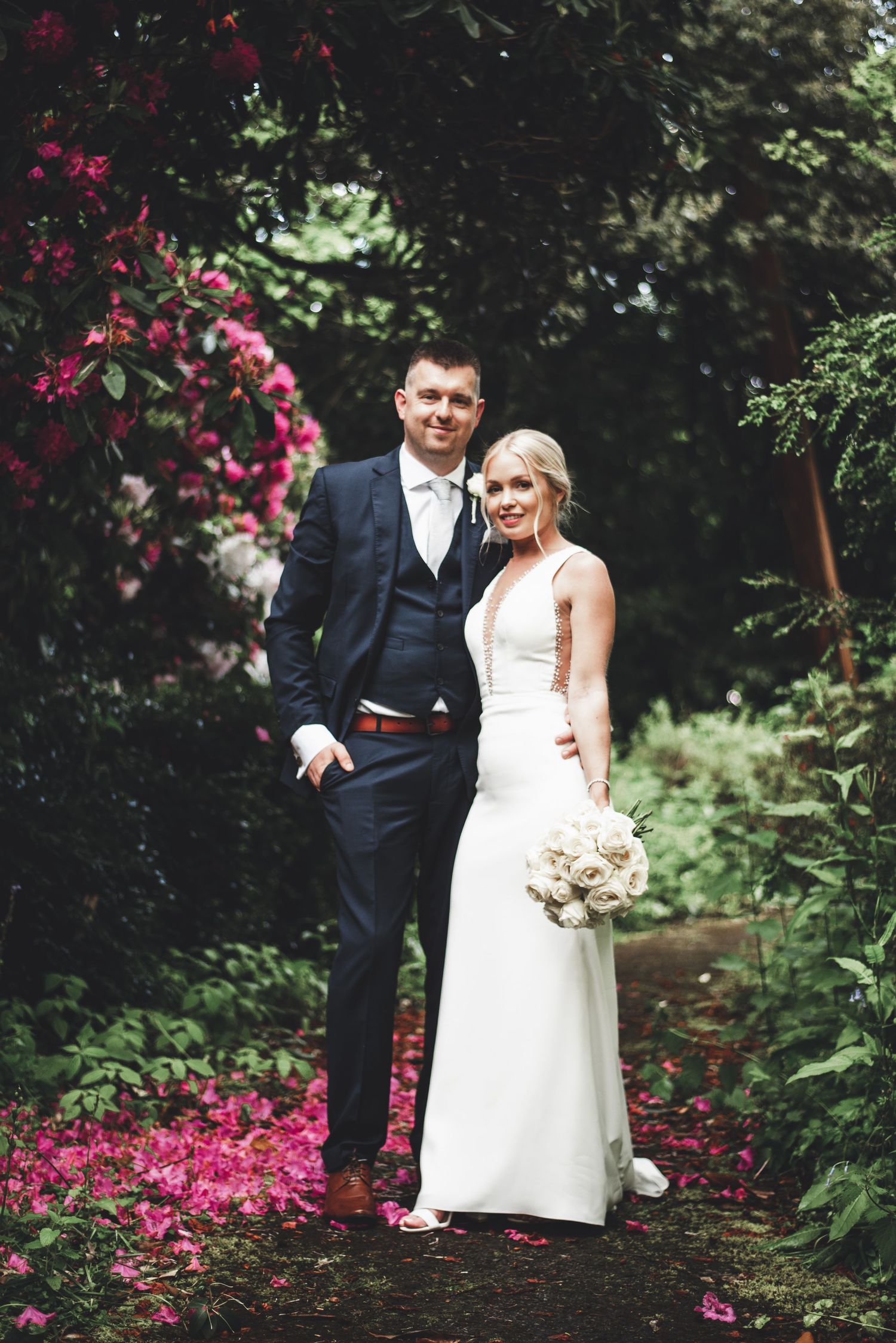 Wedding couple poses in a garden with blooming pink flowers.
