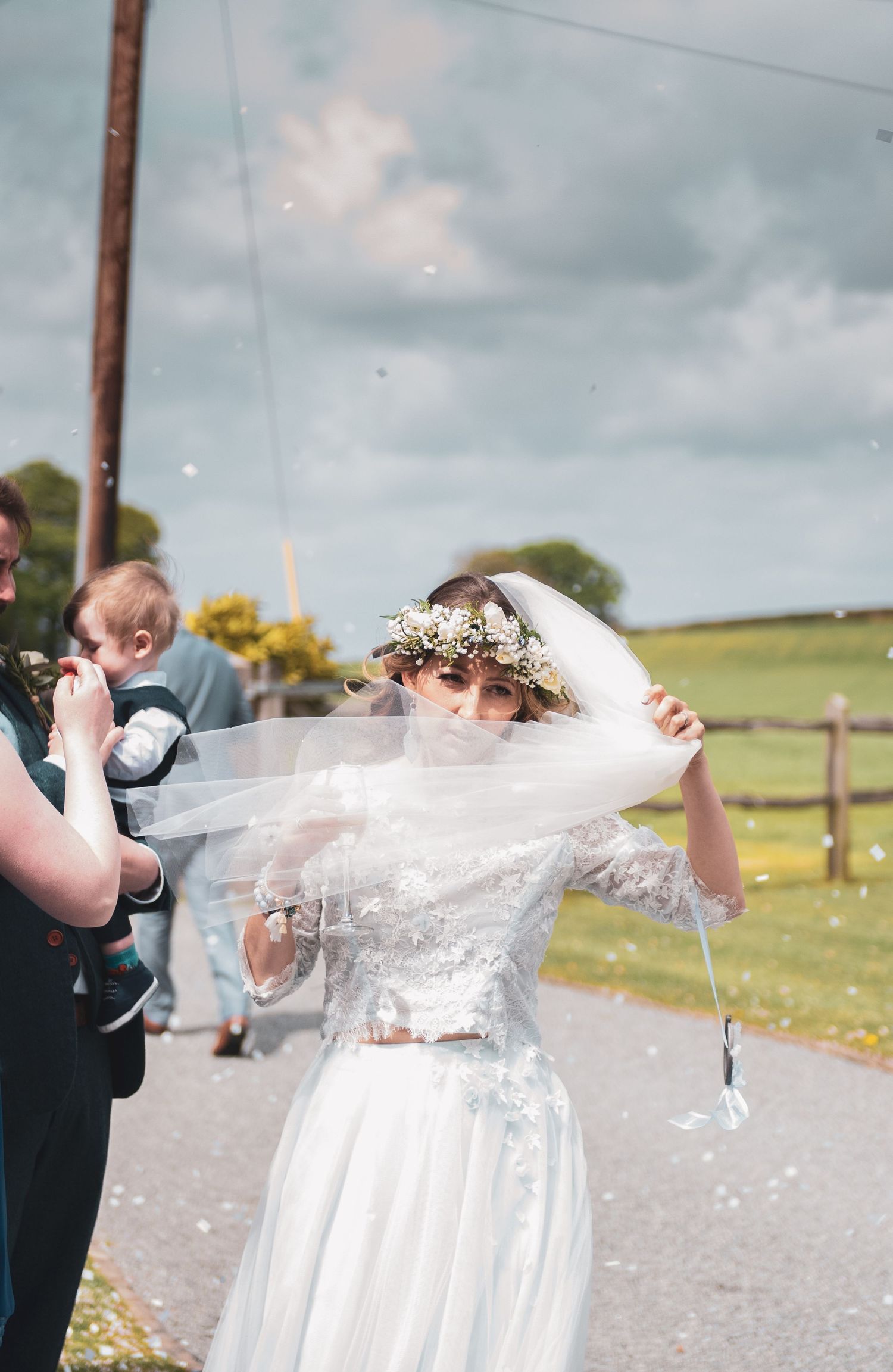 Wedding celebration outdoors with bride adjusting veil in countryside setting.