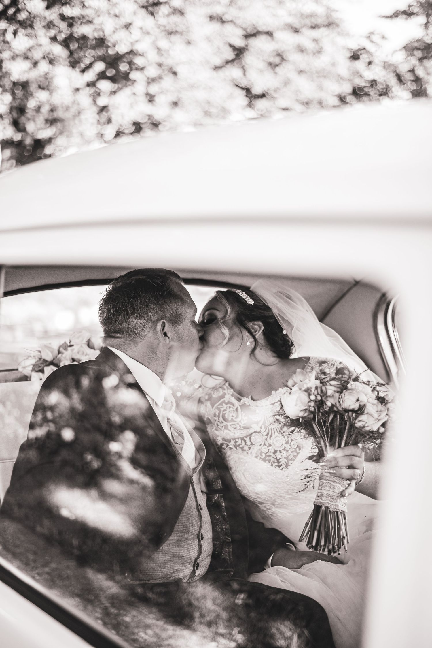 Black and white wedding portrait captured through car window with vintage styling.