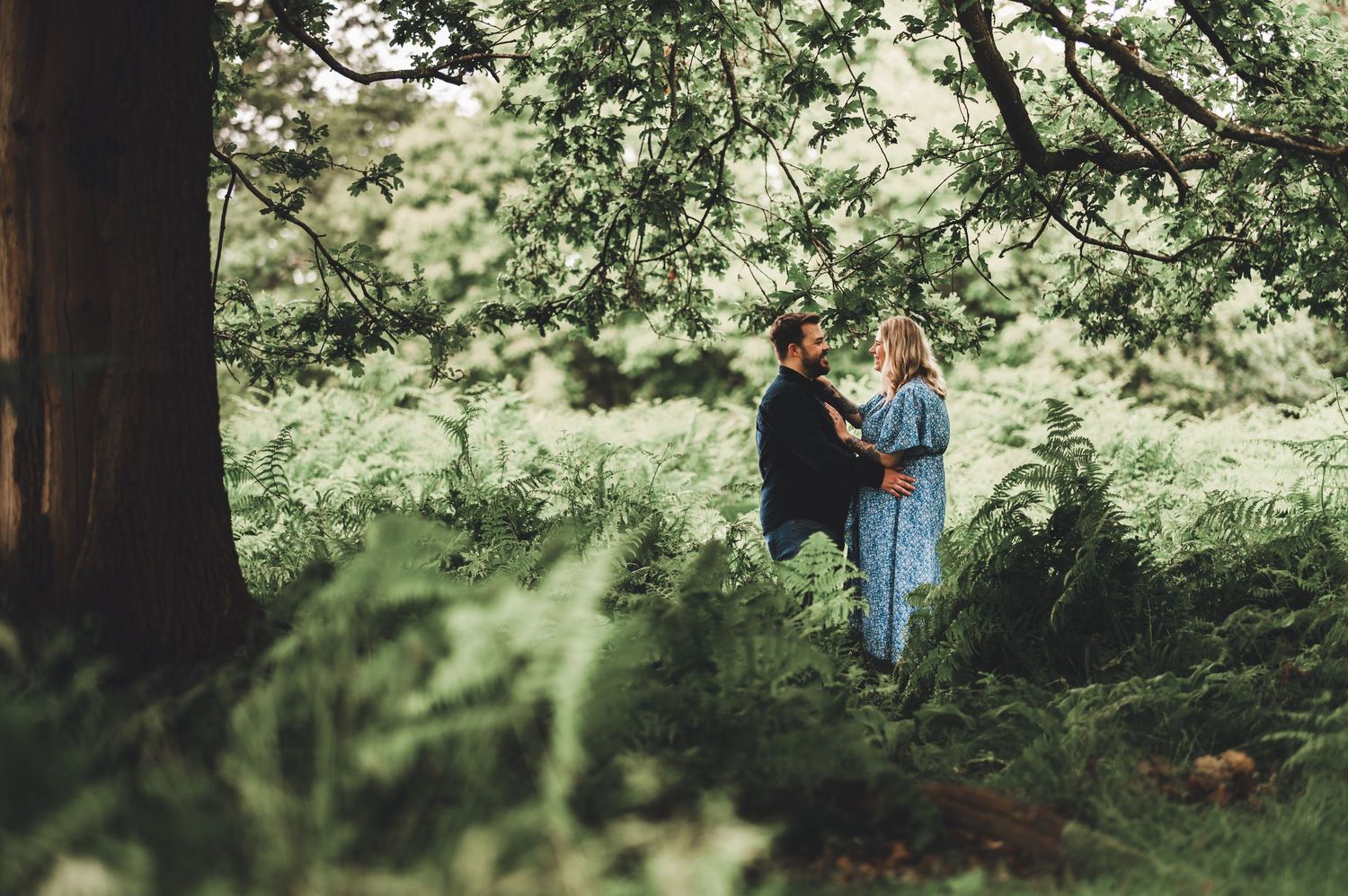 A couple sharing an intimate moment in a lush green forest setting.