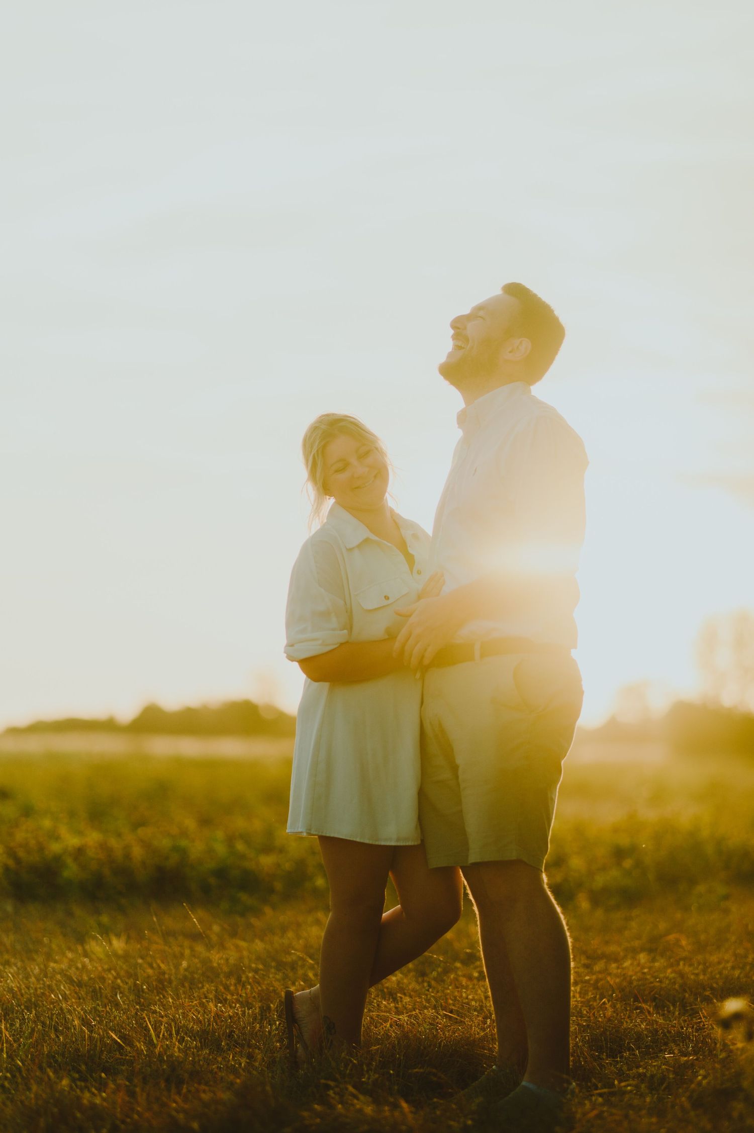 Silhouette of two people embracing in a sunlit meadow at golden hour against bright natural bokeh background.
