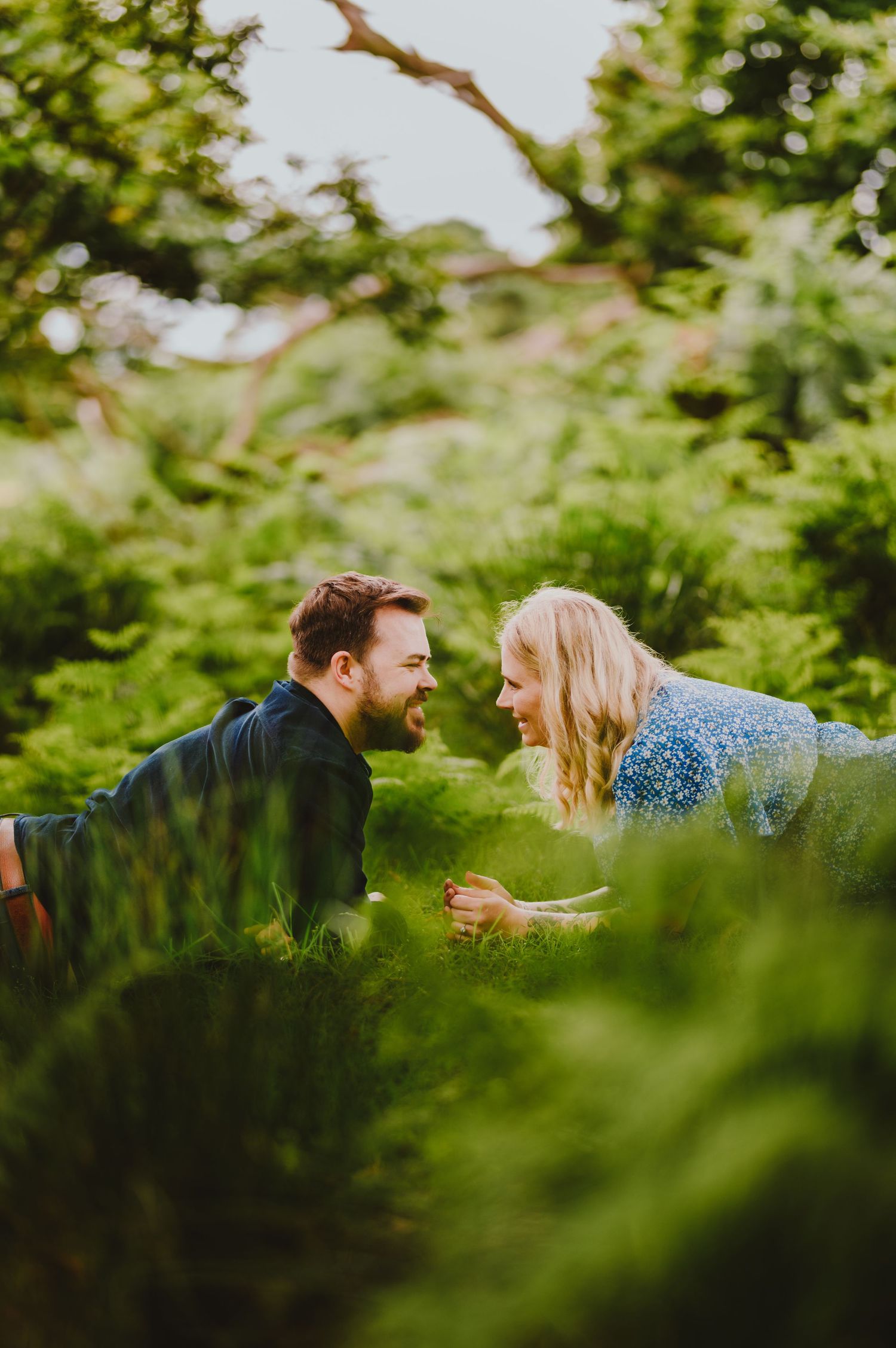 Two people laying in green grass and sharing a joyful moment together on a sunny day among lush foliage.