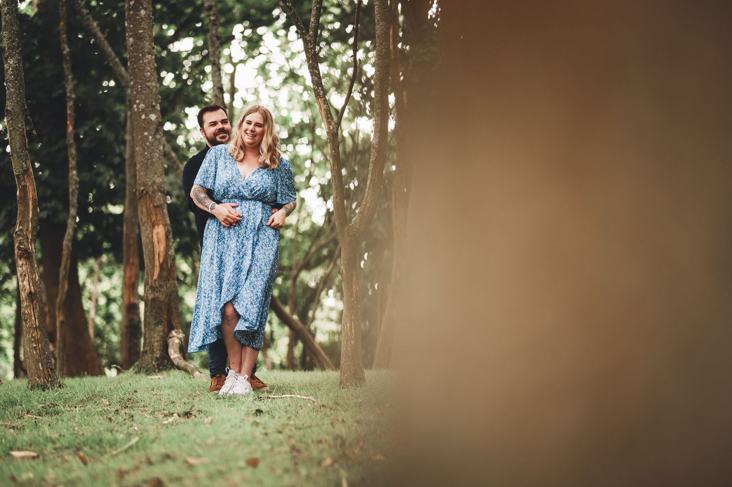 A playful couple runs through a wooded area in casual attire.