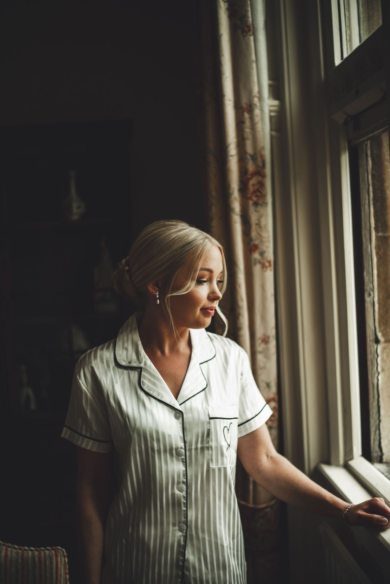 Woman in striped pajamas gazing thoughtfully out of window in morning light.