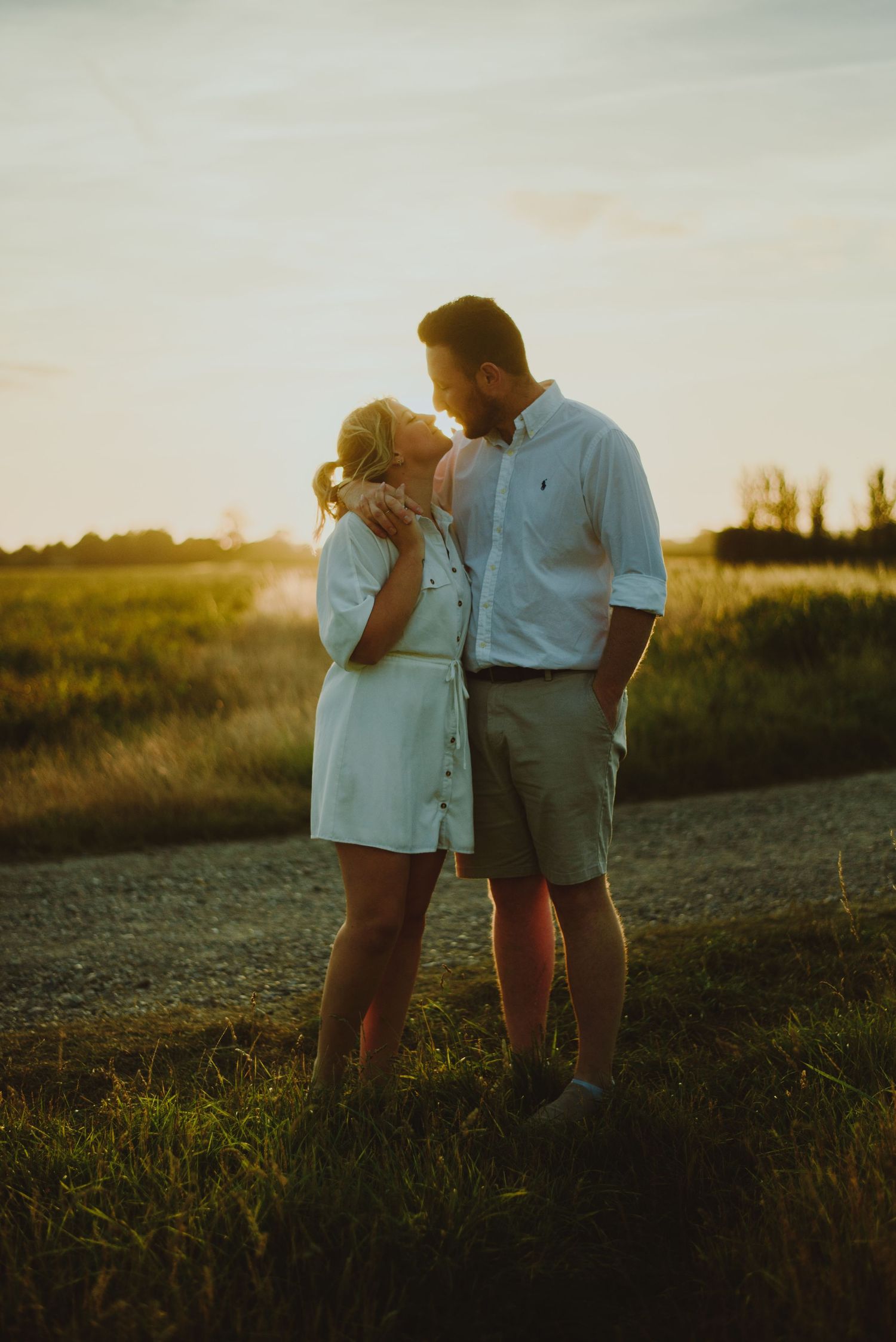 Silhouettes of a couple embrace in a grassy meadow at sunset with warm golden light.