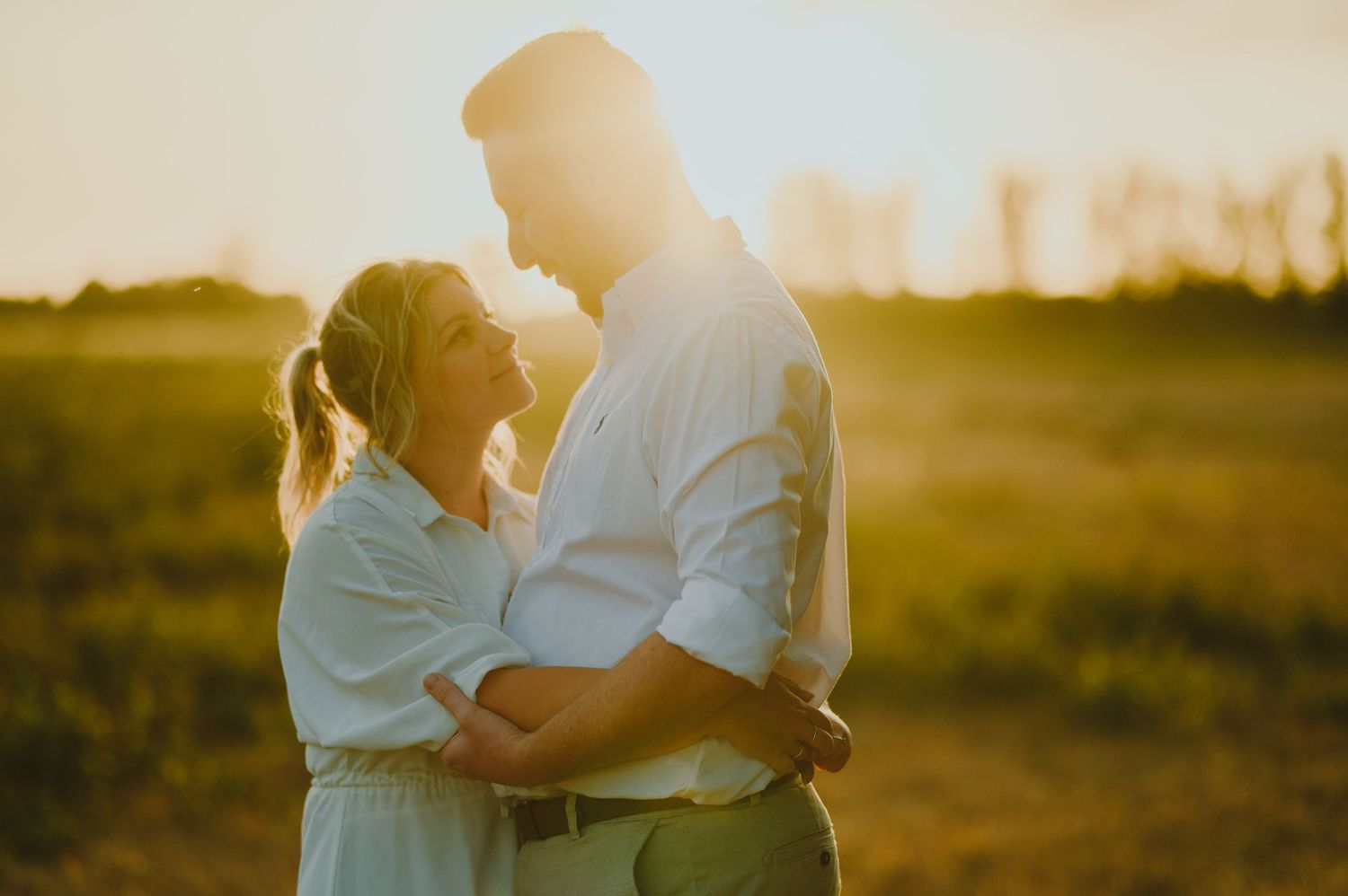 Two people embrace in a golden wheat field during sunset creating a romantic silhouette against the warm sky.