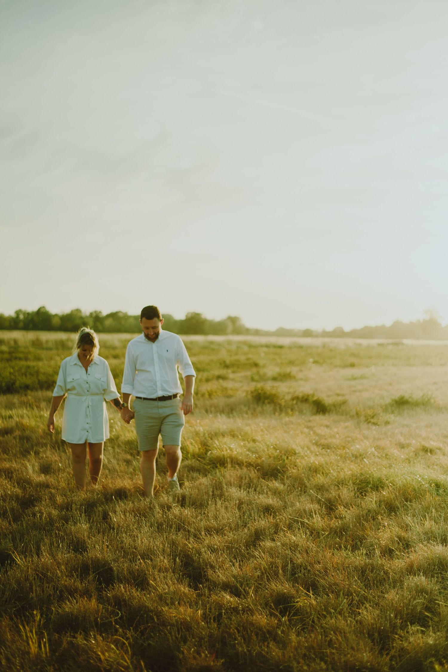 Two people walk together through a sunlit grassy meadow during golden hour.