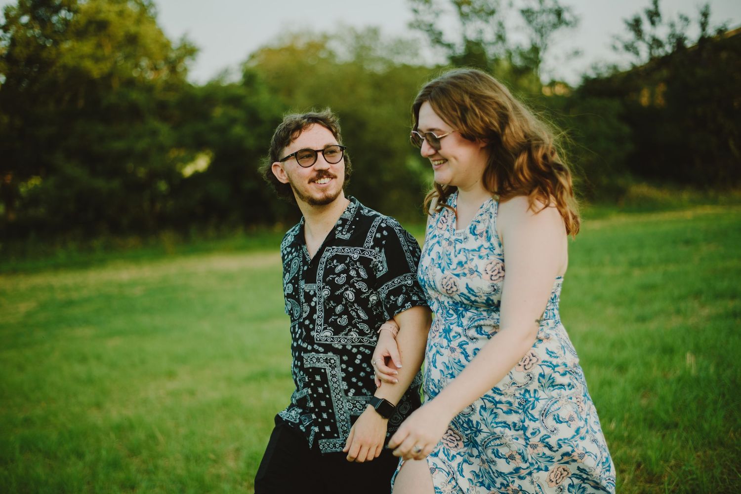 A couple in floral prints share a candid moment together in a lush green field during summer.